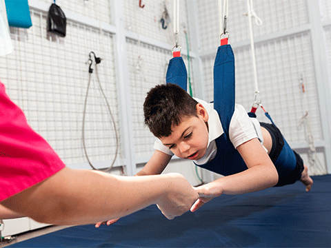 caucasian child doing occupational therapy rehabilitation on elastic cords with therapist