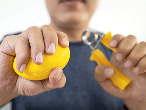 closeup of male patient doing hand, finger, and wrist exercise with rubber ball and spring hand grip